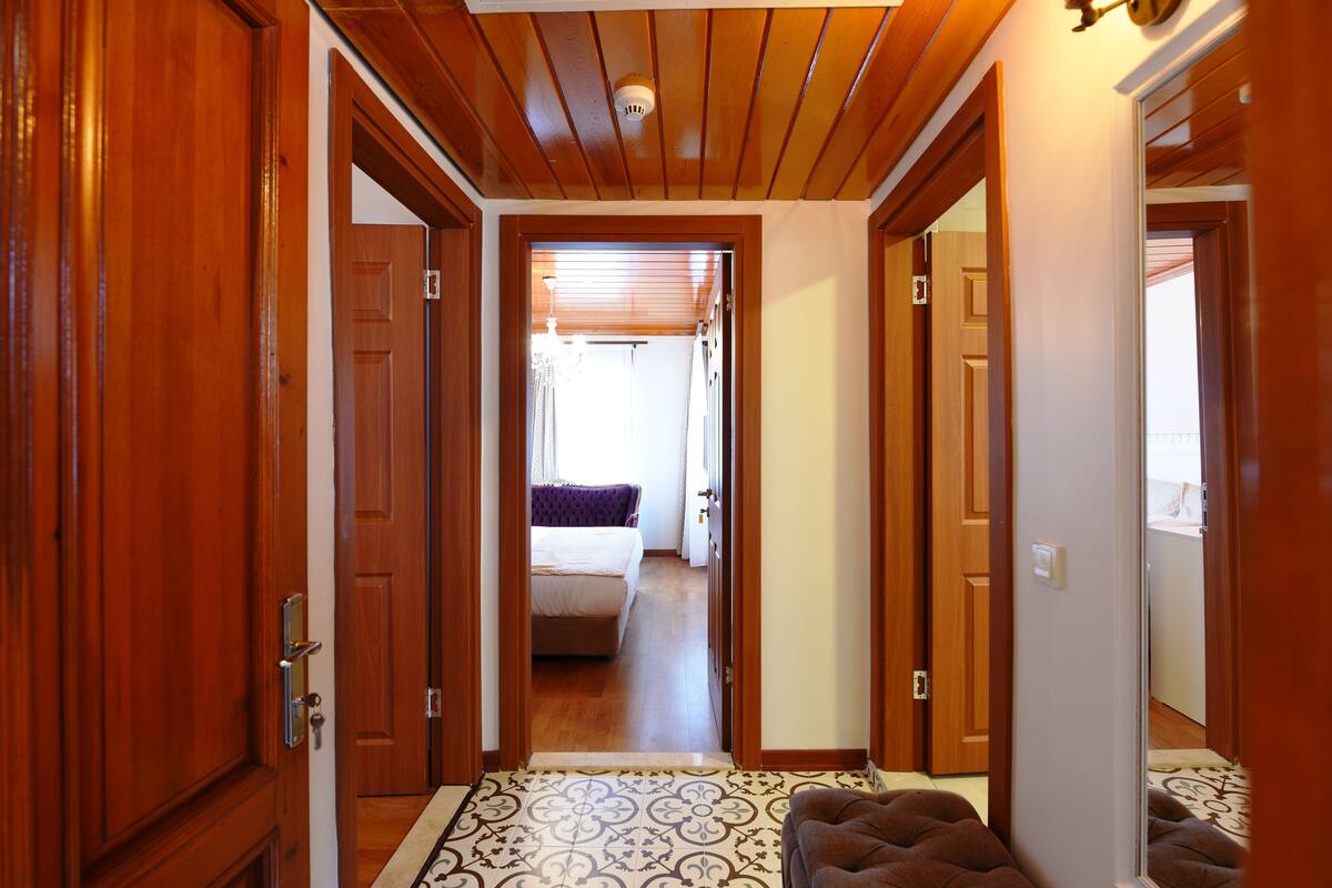 Un couloir avec des portes en bois menant à une chambre à coucher qui contient un lit et une fenêtre.