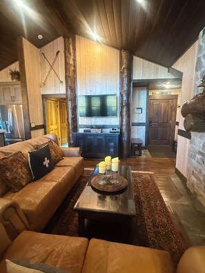 A cozy living room with a leather sofa, a coffee table with candles, and a television mounted on the wall. - Cozy Ski Chalet,  Mountain Views and short walk to base of Deer Valley! (Park City)