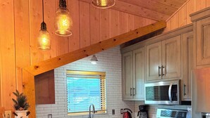 A kitchen with a large island, wooden cabinets, a stainless steel stove, and pendant lighting.