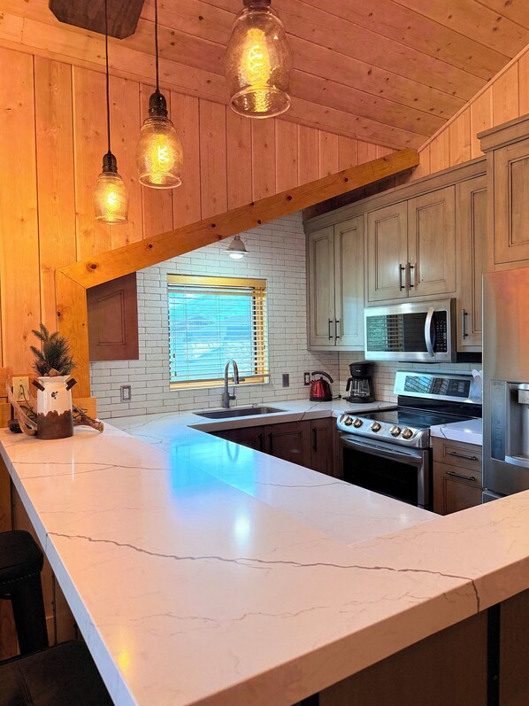 A kitchen with a large island, wooden cabinets, a stainless steel stove, and pendant lighting. - Cozy Ski Chalet,  Mountain Views and short walk to base of Deer Valley! (Park City)