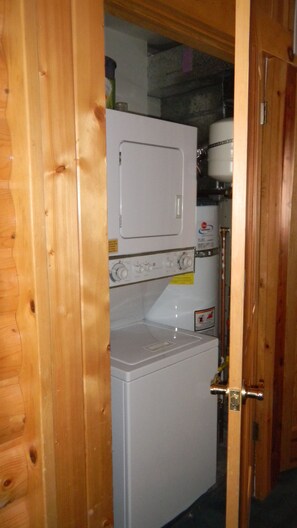 A compact laundry room with a washing machine and dryer, wooden walls, and a visible water heater.