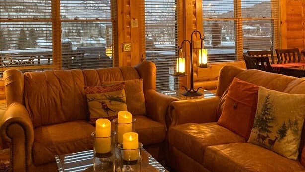A cozy log cabin interior with two leather sofas, a coffee table with candles, and a sign reading "I'd rather be skiing!".