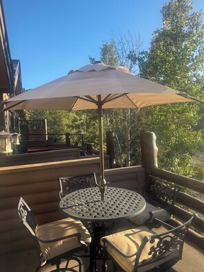 A round table with a woven metal top, surrounded by four chairs with cushioned seats, under a large beige umbrella. - Cozy Ski Chalet,  Mountain Views and short walk to base of Deer Valley! (Park City)