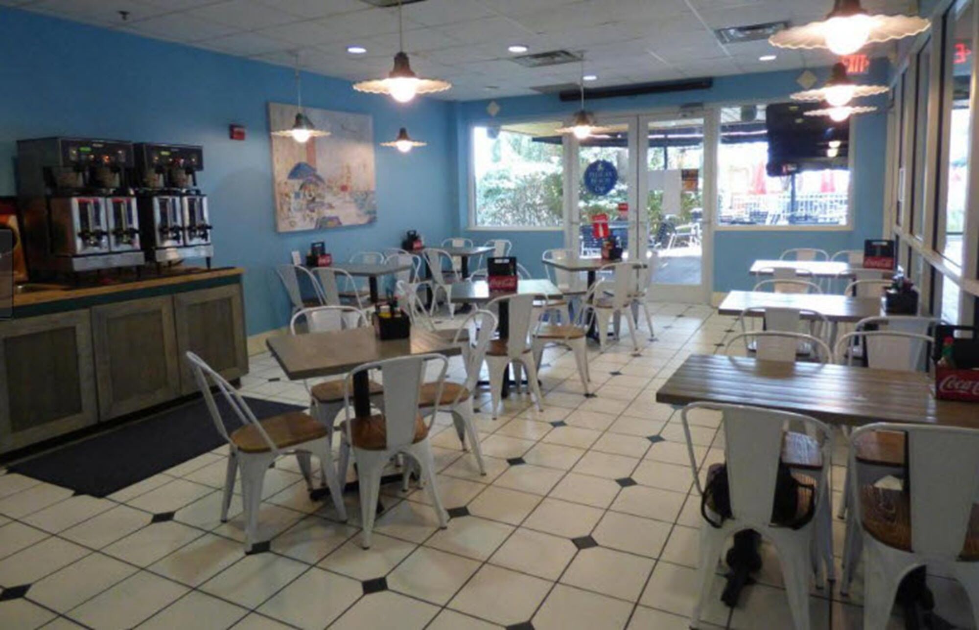 A cafe with white chairs and tables, a tiled floor, and a blue wall with a painting.