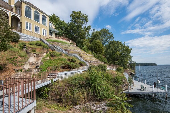 A waterfront property with a stone staircase leading to a wooden deck, a dock with a chair, and a building with large windows. - The Retreat with Wilson Dam view & Water Aces (Florence)