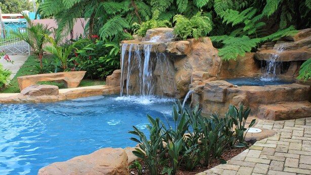 Una piscina con una cascata circondata da rocce e vegetazione.