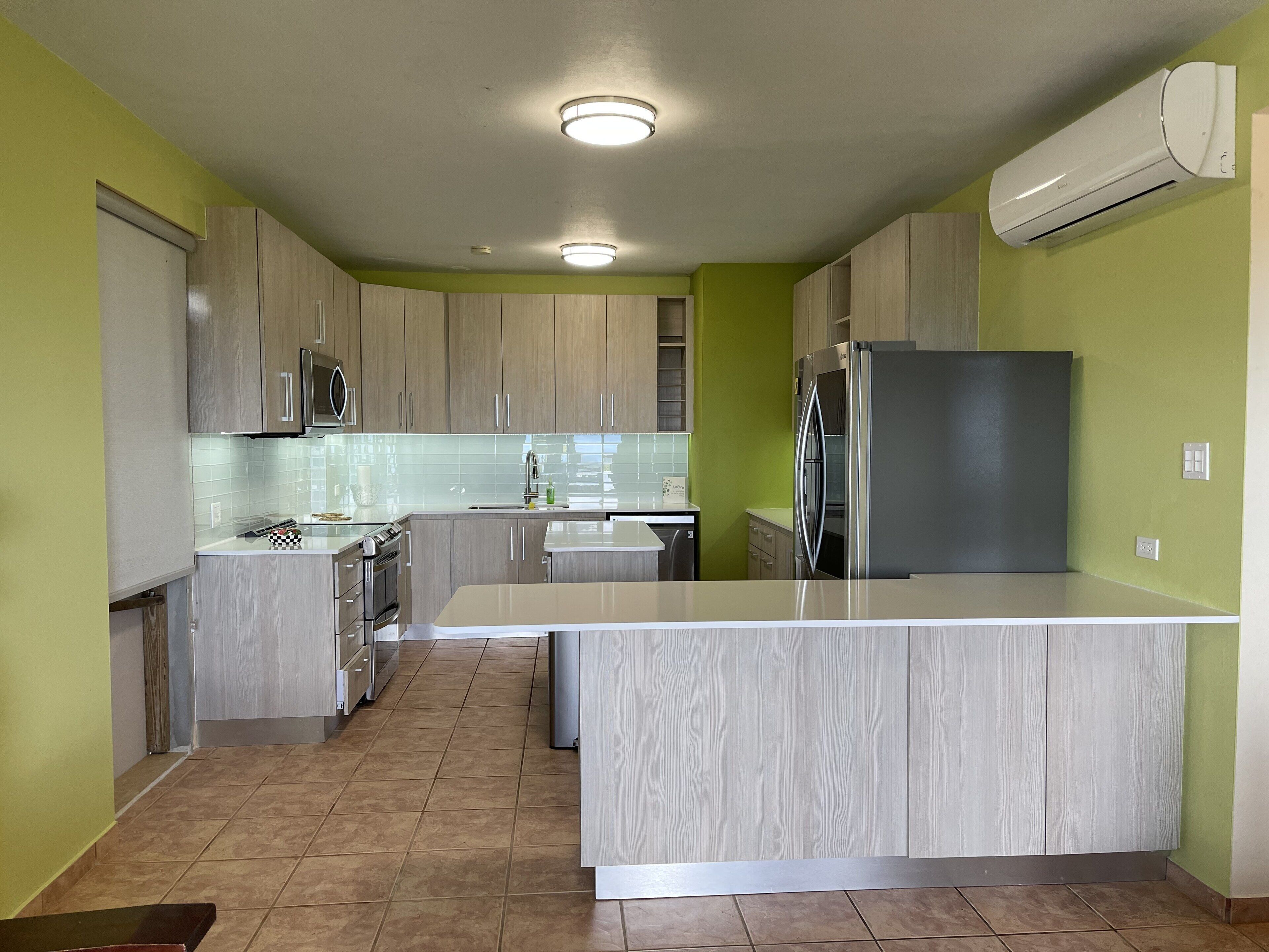Una cocina moderna con armarios de madera clara, una isla central, electrodomésticos de acero inoxidable y paredes verdes.
