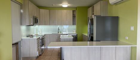 Una cocina moderna con armarios de madera clara, una isla central, electrodomésticos de acero inoxidable y paredes verdes.