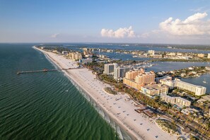 Vista aérea de una ciudad costera con una extensa playa de arena, un puerto deportivo y varios edificios de gran altura.