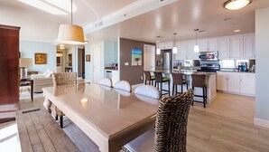 Una cocina amplia con armarios blancos, una isla central y un comedor con una mesa grande y sillas de mimbre.