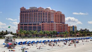 Un gran hotel con múltiples balcones, una torre de salvavidas y sombrillas de playa.