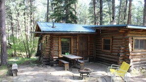 A log cabin with a stone patio, wooden benches, and a fire pit. - Storybook Cottage in the Heart of the Big Horn Mountains (Story)