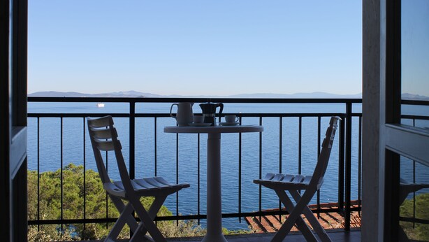 A balcony with two chairs and a table, overlooking a body of water and distant mountains. - Villa Porticciolo (Rio)
