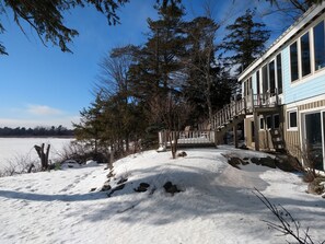 Un sendero cubierto de nieve que lleva a un edificio con grandes ventanales y una escalera de madera.