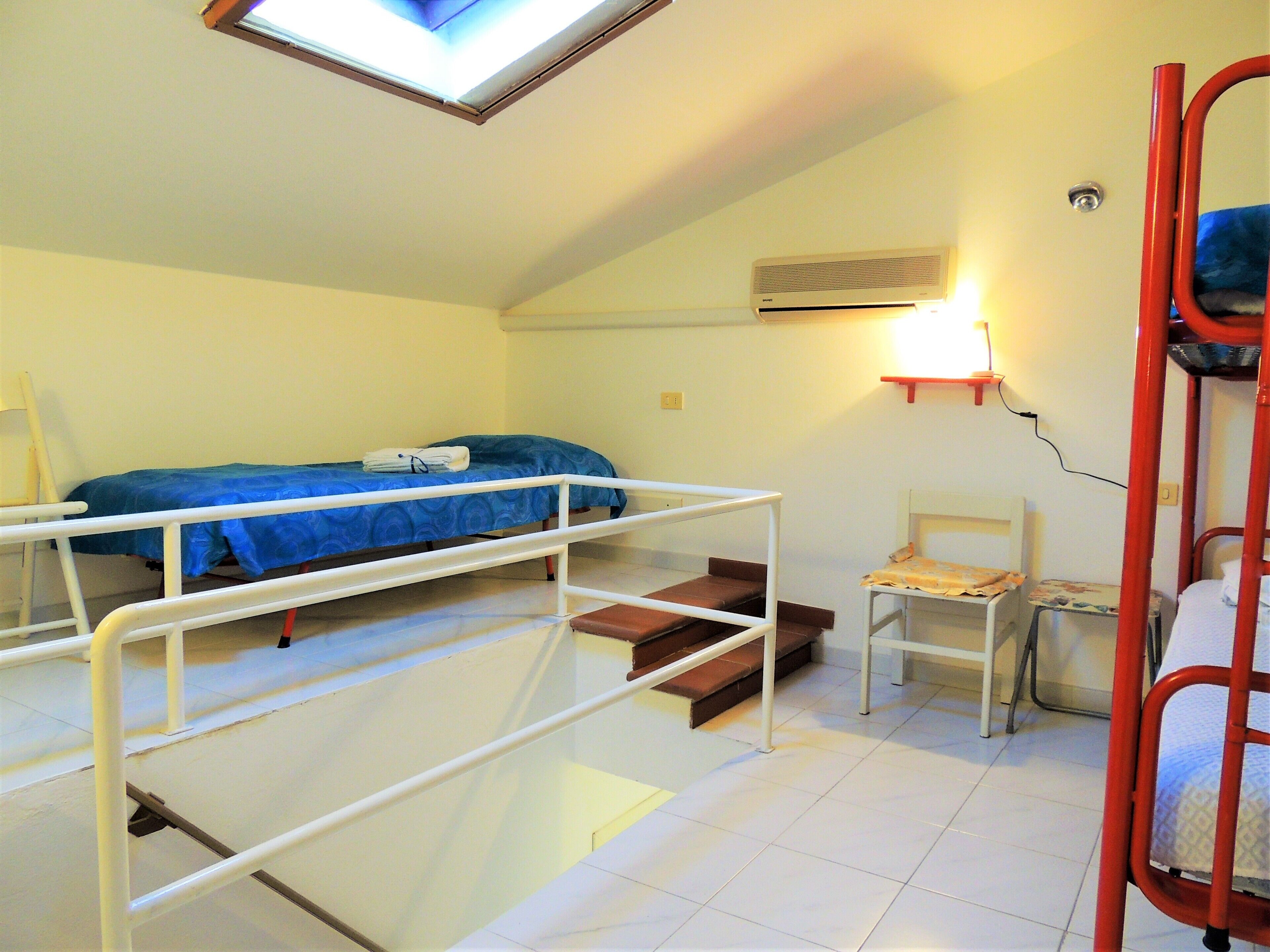 A dormitory room with a bunk bed, a desk, a chair, and a skylight.