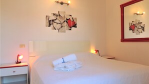 A hotel room with a neatly made bed, a bedside table with a lamp, and a wall-mounted light fixture. - Appartamento Portolongone (Porto Azzurro)