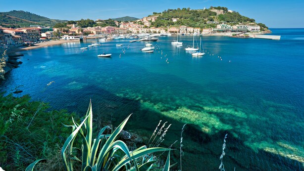 A coastal town with clear blue waters, boats, and a hilltop with buildings. - Appartamento Portolongone (Porto Azzurro)