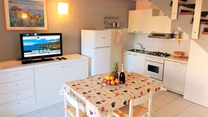 A compact kitchen with a dining table, a refrigerator, a stove, and a sink. - Appartamento Portolongone (Porto Azzurro)