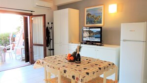 A compact kitchen with a dining table, chairs, a refrigerator, and a television displaying a webpage. - Appartamento Portolongone (Porto Azzurro)