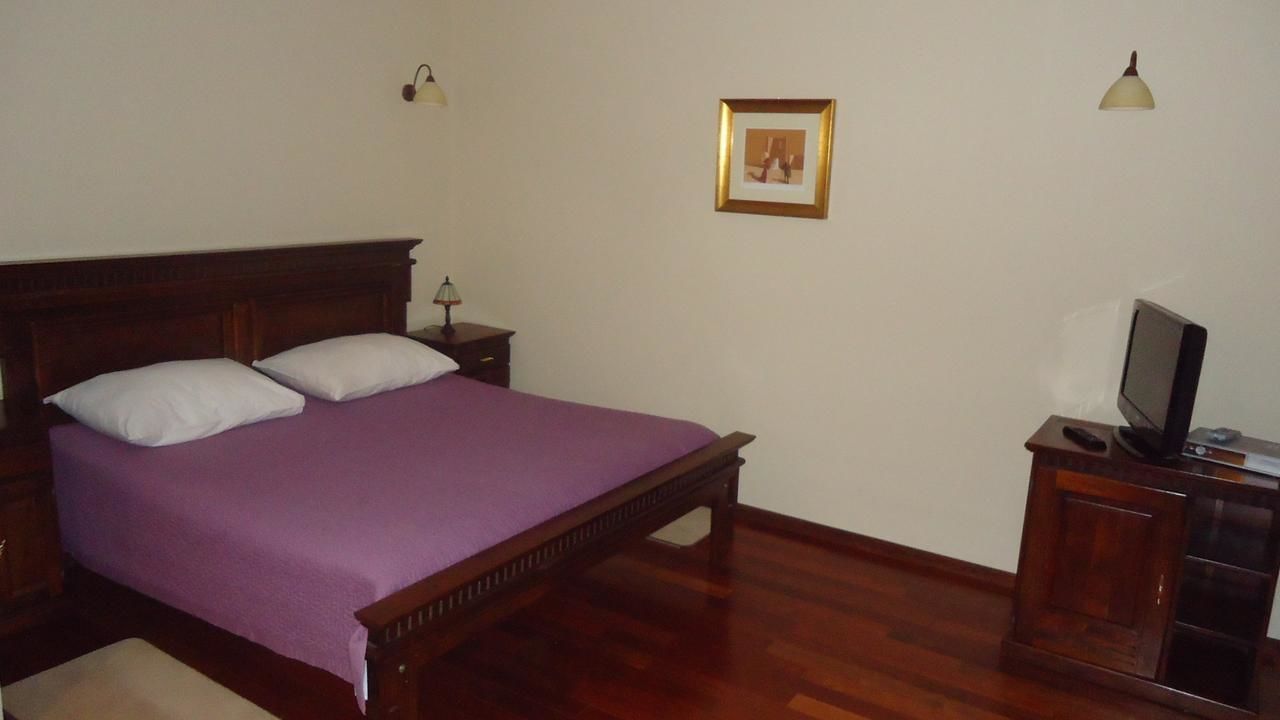 A bedroom with a wooden bed, a nightstand, a TV stand, and a framed picture on the wall.