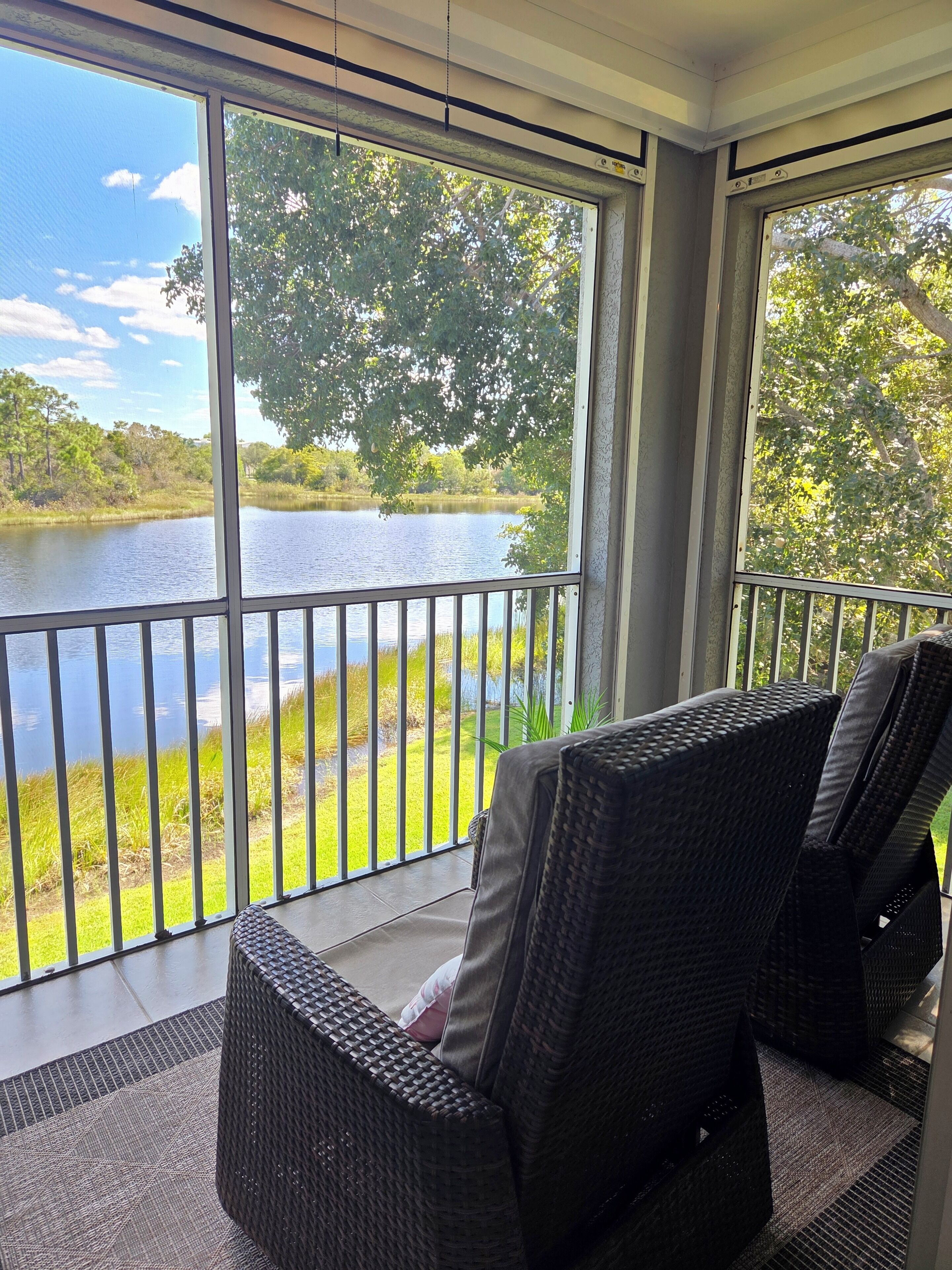 A balcony with wicker chairs overlooking a lake and greenery.