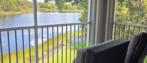 Un balcón con sillones de mimbre que da a un lago y follaje.