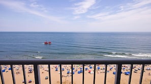 Uma praia com guarda-sóis e pessoas, um barco vermelho na água e um céu claro.