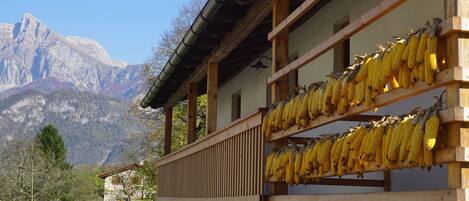 A wooden building with multiple balconies, each holding corn cobs. In the background, there are mountains and a clear sky.
