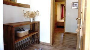 Un pasillo con suelo de madera, una consola de madera con un jarrón de plantas secas, y un espejo en la pared.