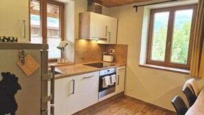 Cocina compacta con encimera de madera, armarios blancos, horno empotrado y ventana con vistas a zonas verdes.