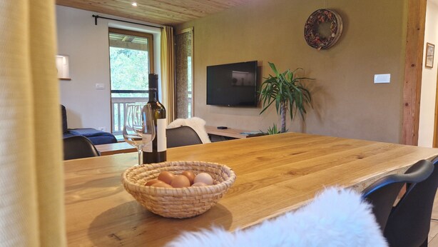 Una mesa de comedor de madera con una cesta de huevos, una botella de vino y un televisor montado en la pared.