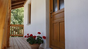 Un porche de madera con una puerta de madera y una planta en maceta con flores rojas.