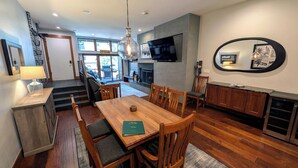 A modern kitchen with wooden cabinets, a dining table, and a TV mounted on the wall. - Luxury Condo w/ FREE WiFi, Parking, Heated Pool, Hot Tubs, Skier Shuttles (Avon)