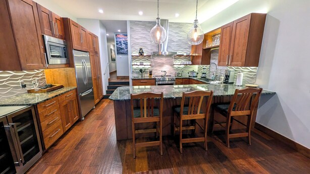 A modern kitchen with wooden cabinets, stainless steel appliances, and a central island with bar stools. - Luxury Condo w/ FREE WiFi, Parking, Heated Pool, Hot Tubs, Skier Shuttles (Avon)