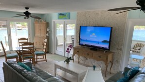 Een woonkamer met een televisie, een bank, een salontafel en een eethoek met stoelen en een tafel.