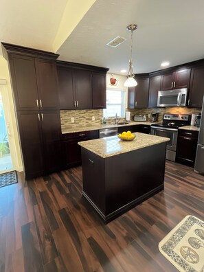 A modern kitchen with dark wood cabinets, a granite countertop, stainless steel appliances, and a patterned backsplash. - Beautifully, Renovated Home in Quiet Cul de Sac! Close to EVERYTHING!  (Oldsmar)