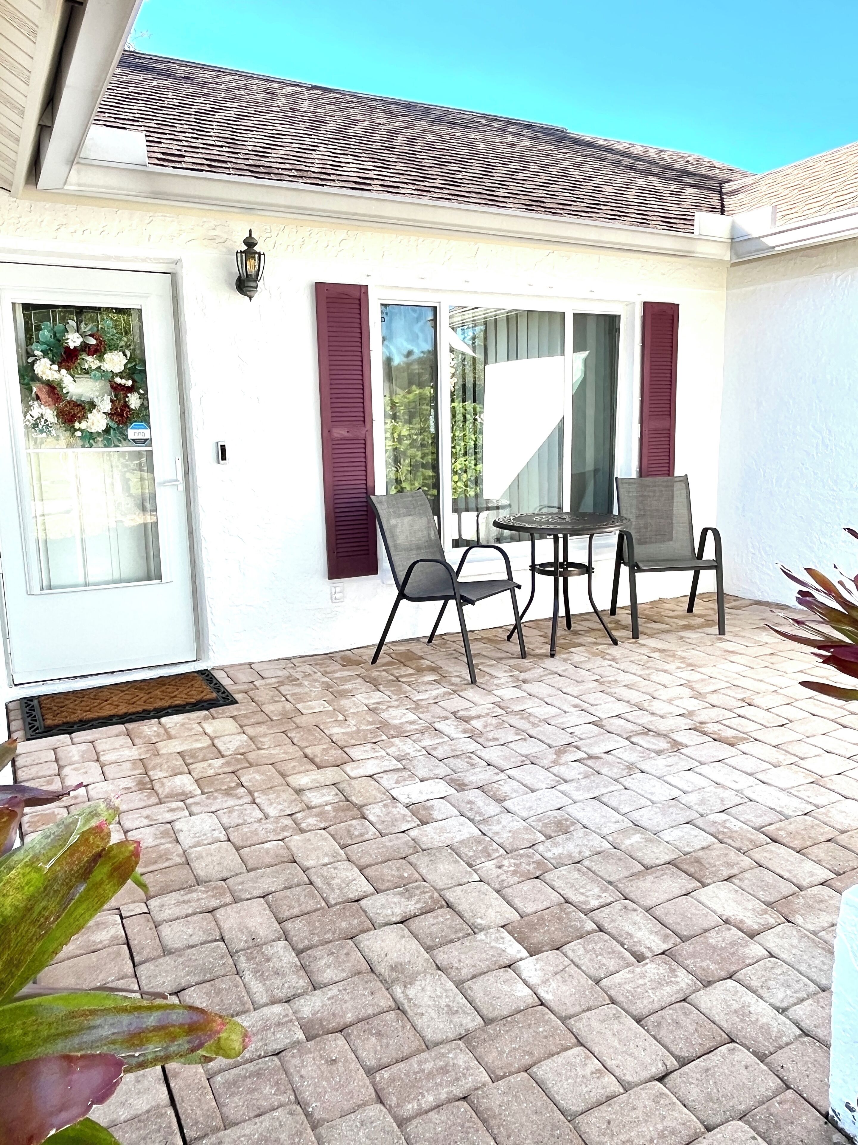 A patio with a table and chairs, a door with a wreath, and a window with shutters.