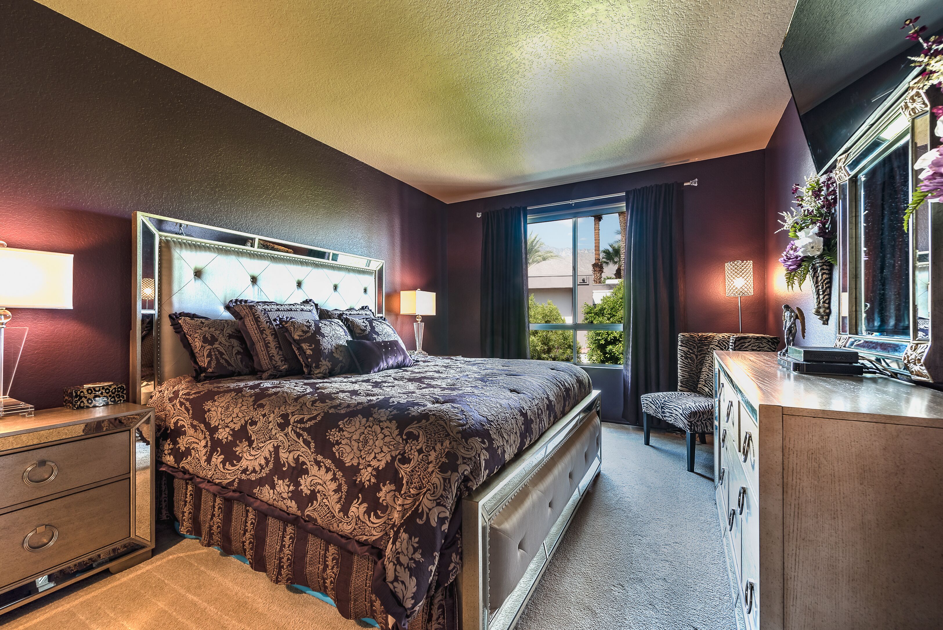 Une chambre à coucher avec un grand lit, des tables de chevet, une commode et une fenêtre donnant sur un paysage verdoyant.