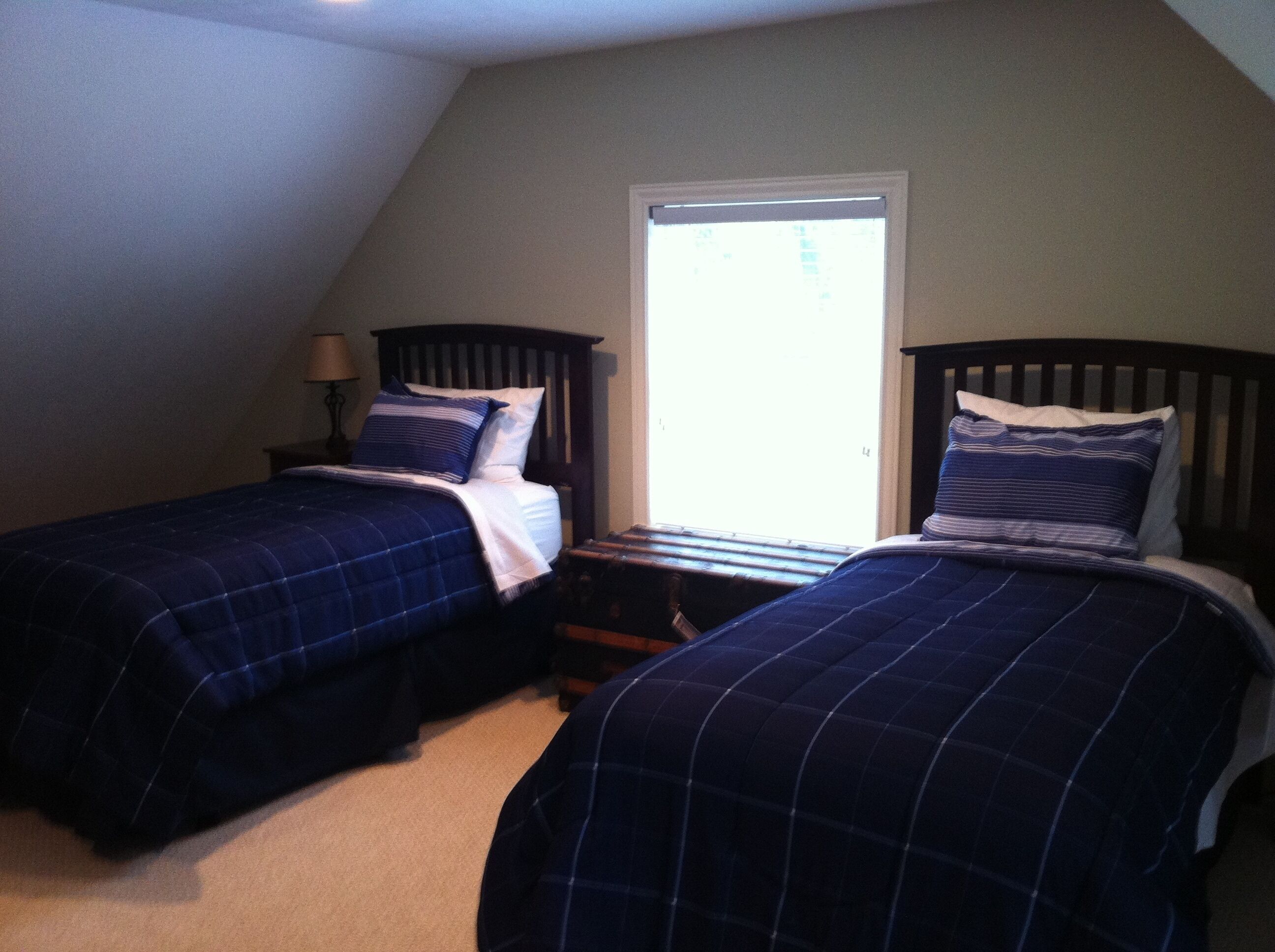 A bedroom with two beds, a window, and a nightstand with a lamp.