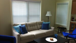 Ein Wohnzimmer mit einem beigefarbenen Sofa, blauen Sesseln, einem Couchtisch und einer Lampe.