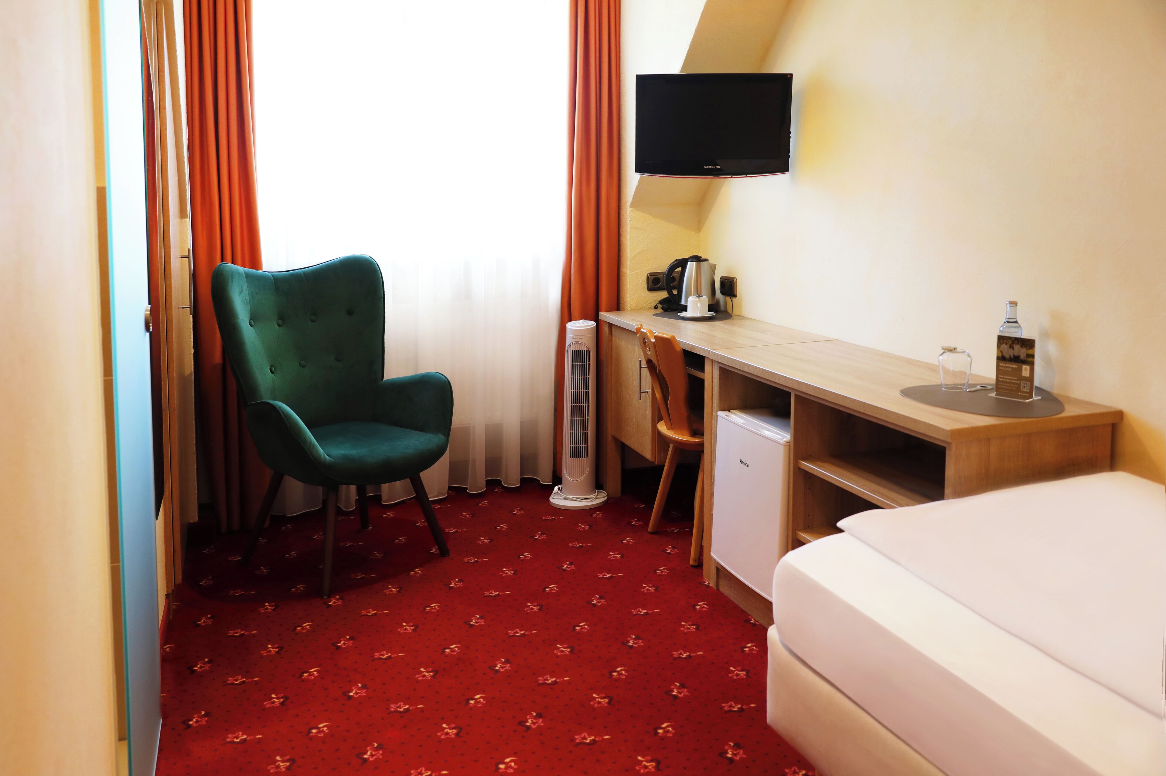 Quarto de hotel com cama, escrivaninha, cadeira, televisão, aquecedor e um pequeno armário.