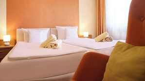 A hotel room with two beds, each with white linens and pillows, a nightstand with a lamp, and a large orange accent wall. - Gasthof Zur Post (Königstein)