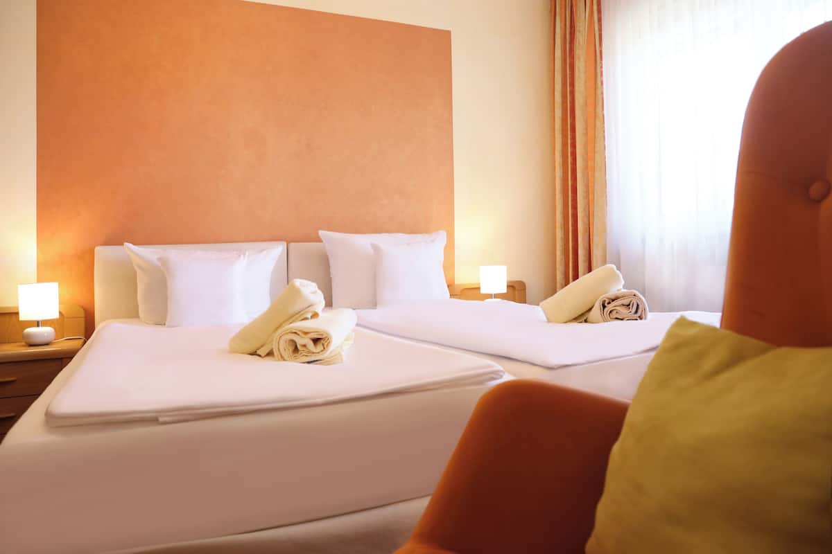 A hotel room with two beds, each with white linens and pillows, a nightstand with a lamp, and a large orange accent wall.