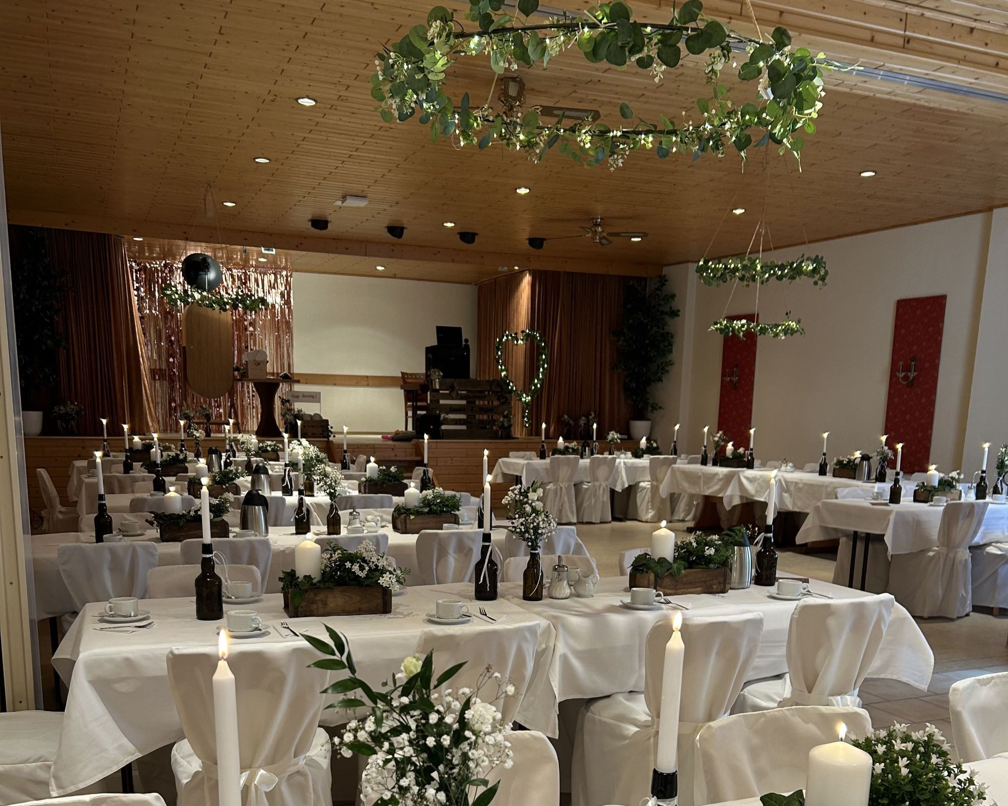 A banquet hall with round tables covered in white tablecloths, candles, and floral centerpieces.
