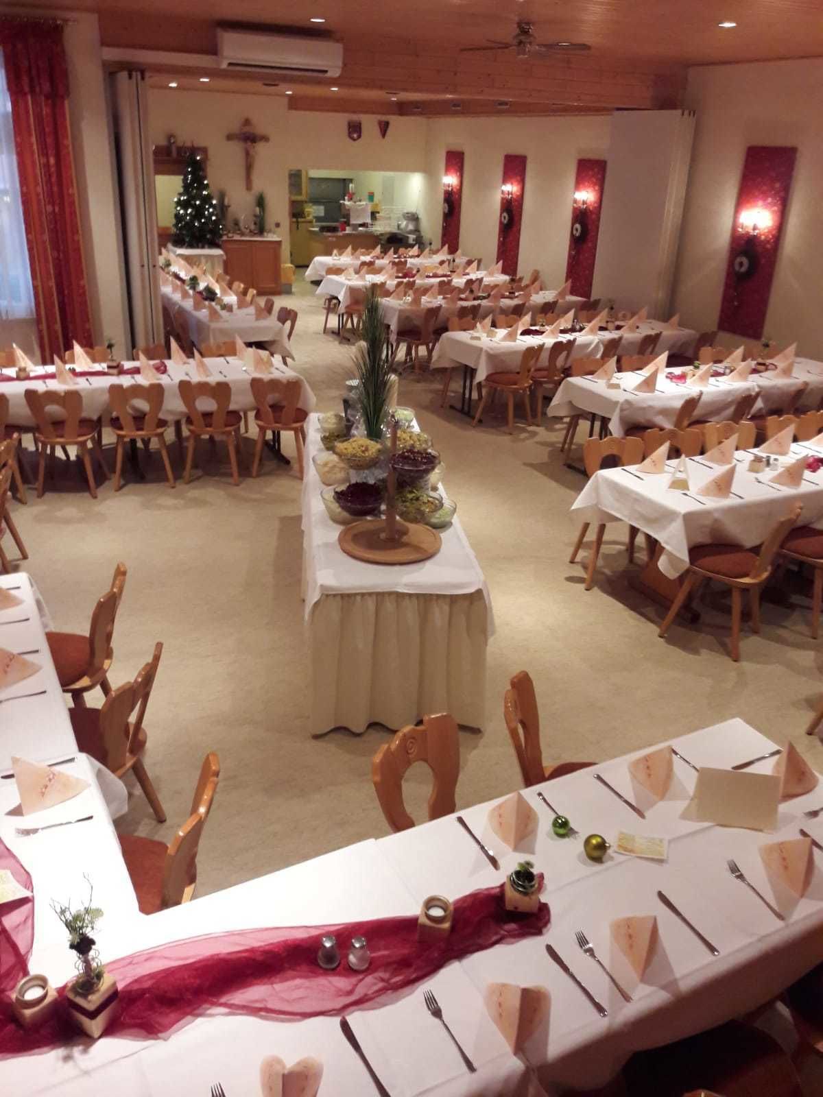 Un salón de banquetes con varias mesas redondas, cada una con mantel blanco, sillas de madera y centros de mesa.