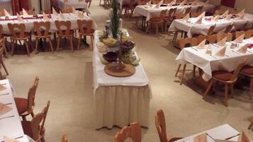 Un salón de banquetes con varias mesas redondas, cada una con mantel blanco, sillas de madera y centros de mesa.