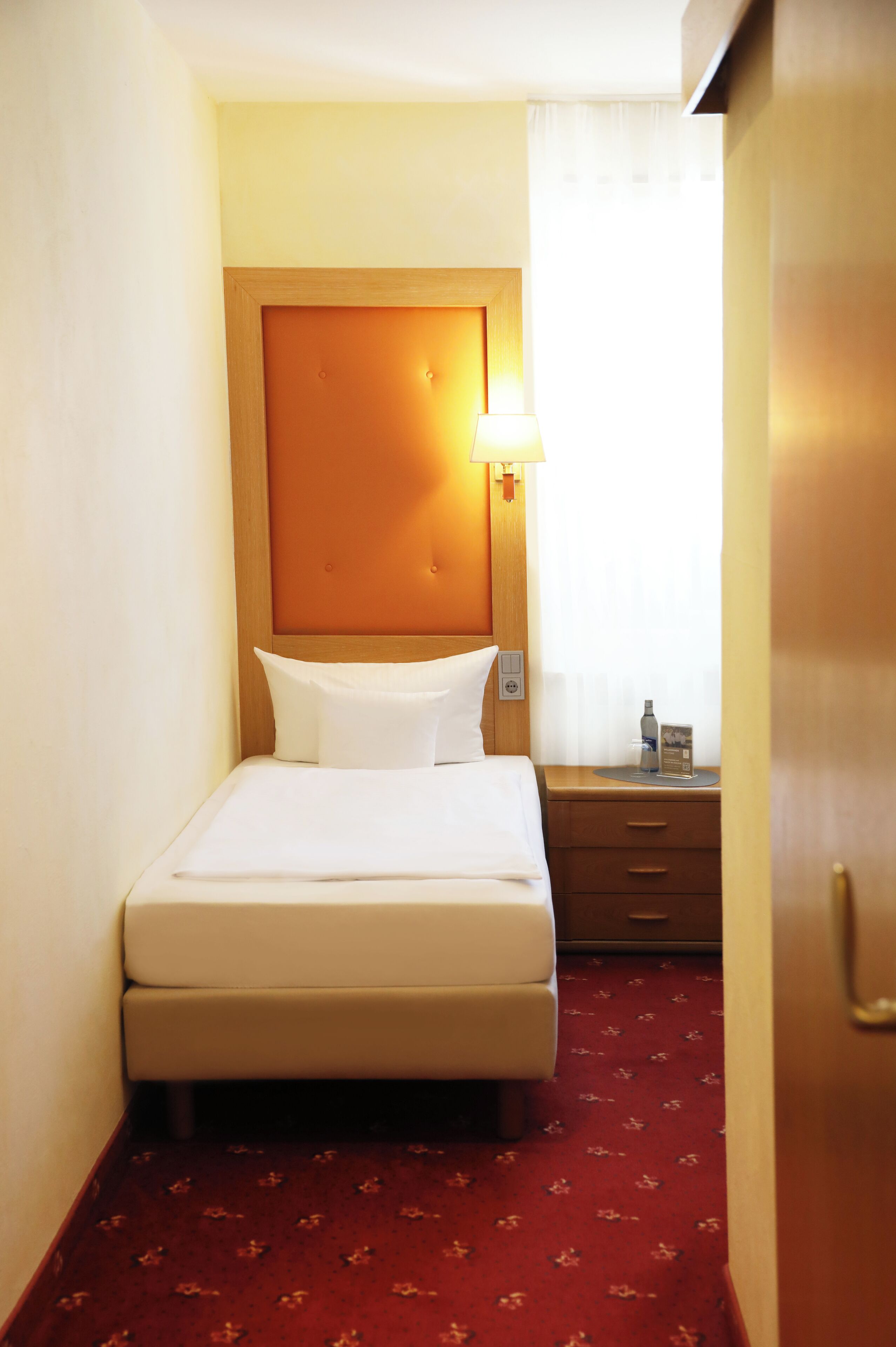 Une chambre d’hôtel avec un lit, une table de chevet, une lampe et une porte.