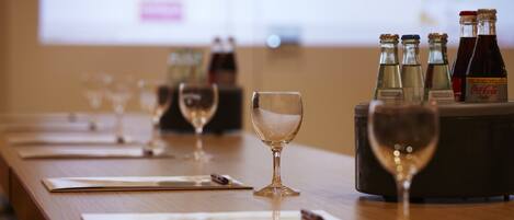 A table with wine glasses and bottles, a projector screen in the background, and a wooden table surface.