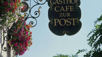 Un cartello con la scritta 'GASTHOF CAFE ZUR POST' e un'illustrazione di una carrozza trainata da cavalli.