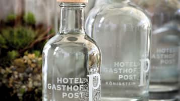Due bottiglie di vetro trasparente con tappi di legno etichettate con "HOTEL GASTHOF POST KONIGSTEIN" e circondate da cubetti di ghiaccio.